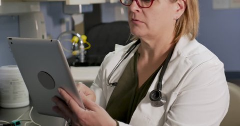 Female doctor filling out patient medical records on a digital tablet health app in a hospital or clinical setting