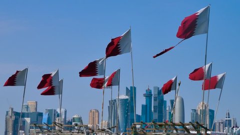 National flag of Qatar waving in wind with Doha downtown and skyscrapers in background