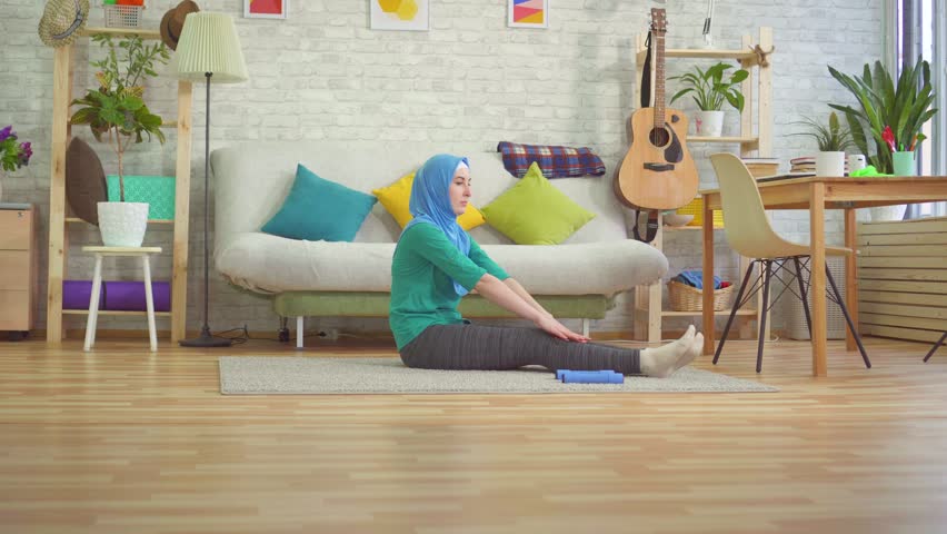 Sporty muslim woman in hijab doing warm-up in a modern apartment