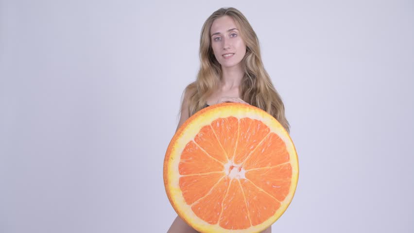 Happy young blonde woman in swimsuit biting orange pillow as healthy concept