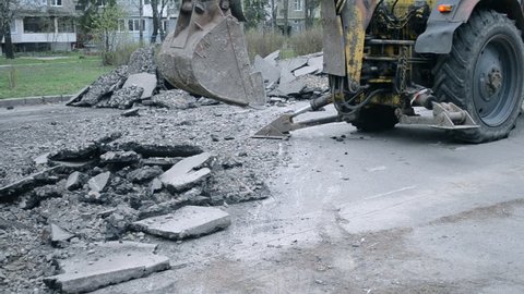Old tractor bucket breaking asphalt. Technical city works. Repair urban work close-up