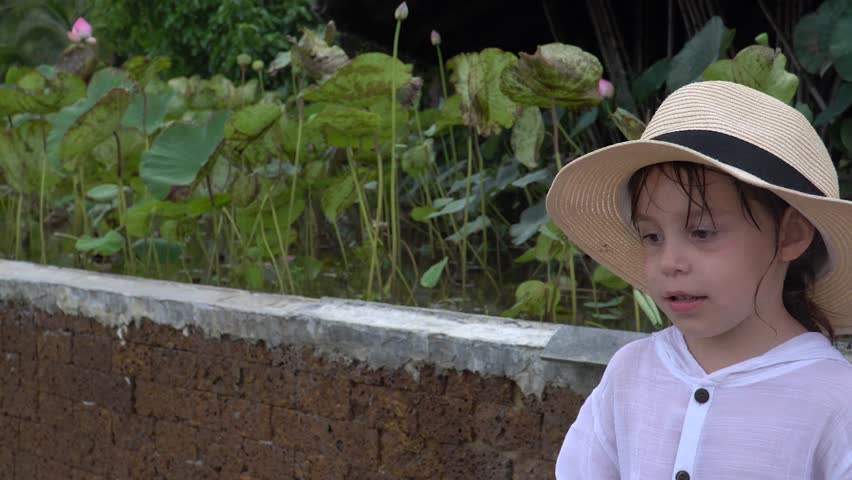 Portrait of a little girl on the background of the park. A child of 5-6 years in a white shirt with blond hair. The kid tells something in the camera.