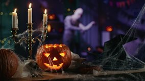 Halloween Still Life Colorful Theme: Scary Decorated Dark Room with Table Covered in Spider Webs, Burning Pumpkin, Candlestick, Witch's Hat and Skeleton.Background: Silhouette of Monster Walking By - Powered by Shutterstock - Get 15% off with code: PIKWIZARD15
