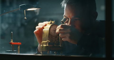 Slow motion close up of a professional watchmaker repairer working on a vintage mechanism clock in a workshop. Shot in 8K.