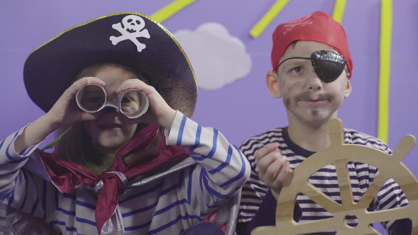 Portraits of two cute children in costumes playing and enjoying in pirate game with props, little girl captain holding spyglass and boy rudder of ship, close up, concept acting and performance, 4k. Royalty-Free Stock Footage #1025266469