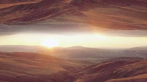 Trippy surreal 4k drone footage of red hills with sun shining at the background.