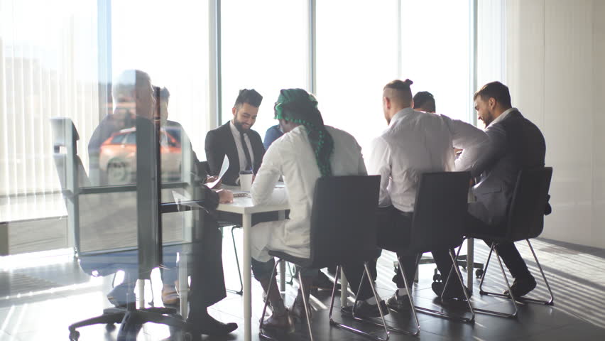 Multiracial team of business partners of different age interacting in boardroom of modern spacious and well-lit office, being viewed through transparent glass wall. | Shutterstock HD Video #1025276036