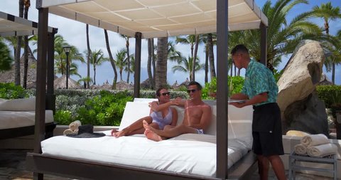Couple Gets Drinks on Bed Poolside at Tropical Resort Pool