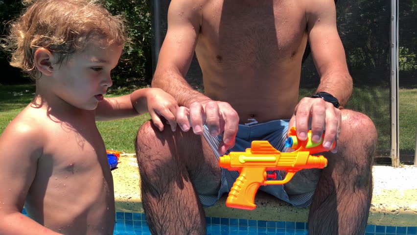 Father showing toddler son how toy works at the swimming pool. Parent teaching child