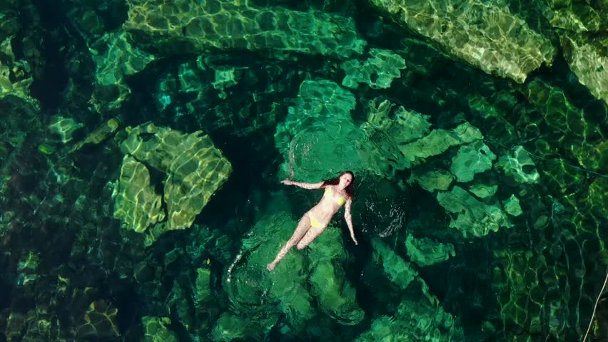 Young brunette woman floats and plays in a natural pool of a cenote in Mexico. | Shutterstock HD Video #1025299283