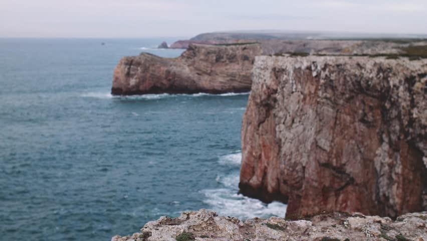 Woman Looking At The Ocean, Standing On The Cliff Edge. SLOW MOTION. Traveler Girl in yellow raincoat relaxing, thinking, dreaming, enjoying nature. Peace and calm landscape.