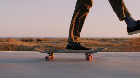 Slow motion cinematic close up of authentic and trendy skateboarder stroll through sunset filled california vibes promenade on warm summer evening. Outdoors activity. Dreamy teenage mood