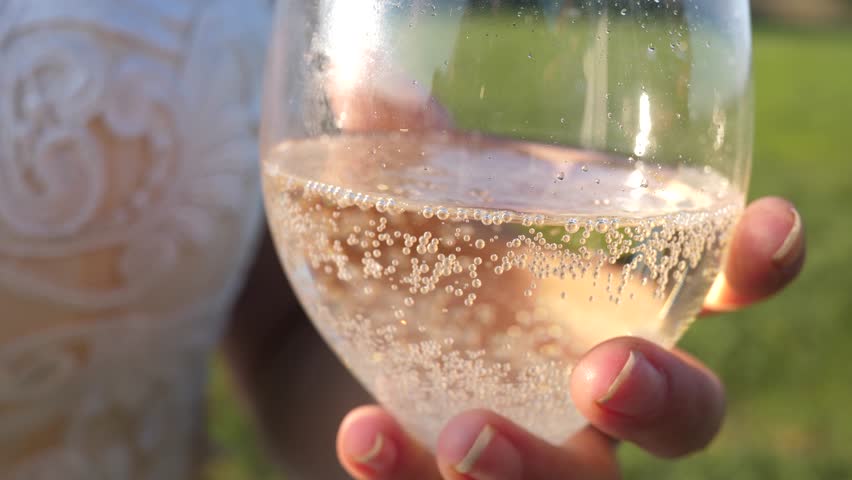 pouring sparkling wine glasses from bottle into transparent wine glasses. close-up. teamwork of loving couple. celebrating success and victory. champagne sparkles and foams in sun. Slow motion