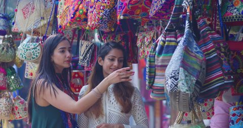 4K Female friends chatting & shopping for handbags in Indian street market. Slow motion.