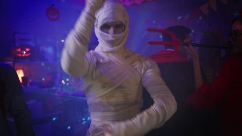Halloween Costume Party: Old Skinny and Bandaged Mummy Dances. In the Background Zombie, Death, Witch and She Devil Have Fun in a Monster Party Decorated Room. Shot on 8K RED 