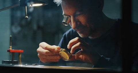 Slow motion of a professional watchmaker repairer working on an old vintage pocket watch in a workshop. Shot in 8K.