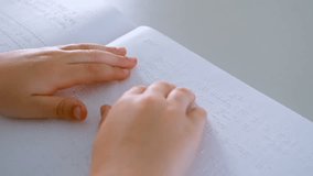 Close-up of blind Caucasian schoolboy hands reading a braille book at desk in classroom at school. He is touching and feeling 4k - Powered by Shutterstock - Get 15% off with code: PIKWIZARD15