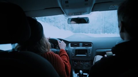 Young couple of travelers and adventurers drives small car or camping van through winding snow covered mountain road on cold winter vacation day. Man makes photos with smartphone of views and girl