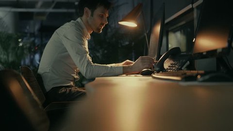 Man Working In Modern Office At Night On Computer.Office Worker Overtime Work In Internet.Businessman Working Alone.Graphic Designer Overworked On Computer Late Night.Workaholic Pc Overtime Deadline 