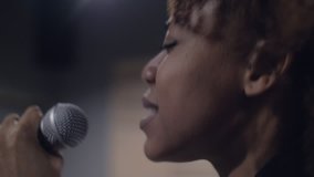 Close up of one young African female singer singing in the studio with a microphone in hand. Side view of African American woman singer musician on stage performing 4k clip