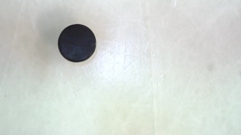 Hockey puck spins and falls on the ice in slow motion and stick hitting it, top view