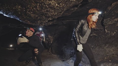Group of people with bright headlamps entering dark cave and touching stone surface during speleology expedition
