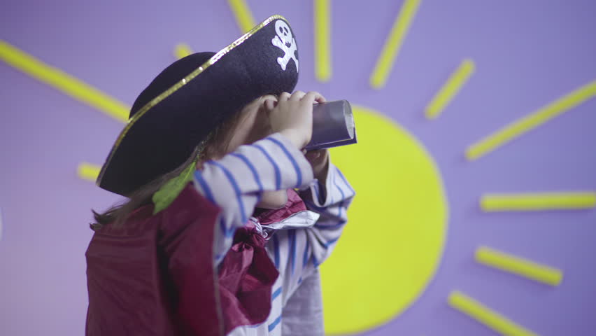 Little girl in costume captain of pirates looking through binoculars, portrait of female child with spyglass, close up, sun as decoration in the background, kid playing game and performing show, 4k. Royalty-Free Stock Footage #1025348222