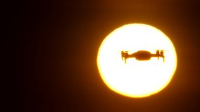 Popular consumer drone stay in air, silhouette against large sun disc, copy space version of footage. Little modern copter hover on place, slow motion telephoto shot