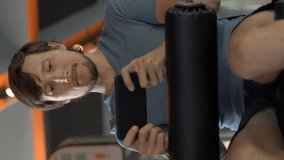 Vertical video. A young man at the gym on an exercise bike holding the phone in front of his eyes in his hands. All the attention is in the phone. The concept of dependence on social networks. Mobile