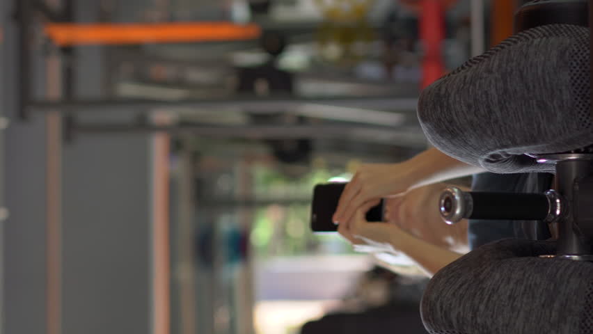 Vertical video. A young woman at the gym doing exercises holding a phone in front of her eyes in her hands. All the attention is in the phone. The concept of dependence on social networks. Mobile
