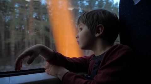 The boy stands at the train window and looks out the window at the running landscapes. Travel by train. Tourism on vacation, travel around the world. Kid traveling by train, dreaming about something.