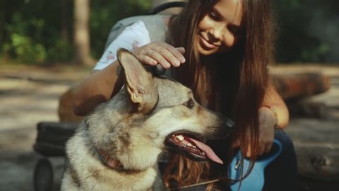 Beautiful happy young woman stroking her loving dog in the forest.