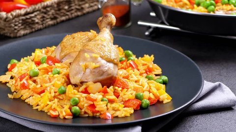 Arroz con pollo. Baked pieces of chicken with bone, rice with paprika and peas. Black background. Served on black plate or spanish pan.  Cooking, steaming, eating, watching. Slow motion.