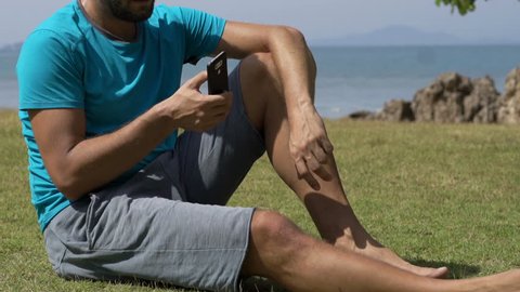 Sporty man texting on smartphone in garden by the sea
