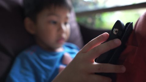 4K young asian boy in the living room using digital tablet to play internet online games. Thumb finger clicking and moving on touch screen. 