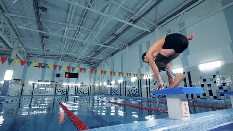 Swimmer with prosthetic leg jumping into a pool, back view.