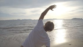 Sportive young man stretching on beach after morning jogging, beautiful sunlight reflecting on sea surface. People sport body conscious concept- SLOW MOTION