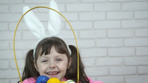 Cheerful child with a basket of Easter eggs. Charming little girl in rabbit ears with a basket of eggs.