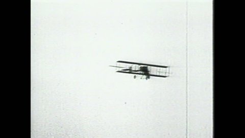 1990s: Men wind propeller on experimental aircraft. Wright Brothers plane rolls across ground. Wright Brother's plane flies through sky. Squadron of military bombers soars through sky.