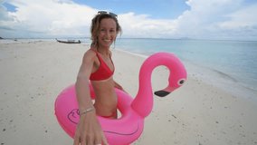 Follow me concept woman leading boyfriend on idyllic beach with inflatable flamingo playing in pristine clear water in the Islands of Thailand. People travel luxury fun and cool attitude concept -