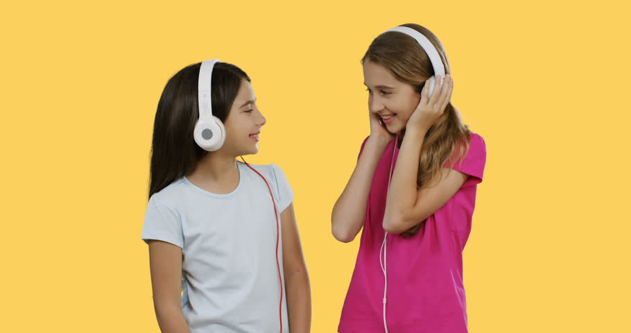 Cheerful teenage girls in the headphones listening to the music and dancing on the yellow screen background.