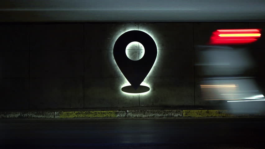 Big glowing sign of geolocation. Endless stream of cars. Check-in. Time-laps. Trip around the world. geotag. A point on the map. Navigation. Night city. Location of a person.