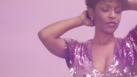 black mixed race woman with short haircut and curly natural hair wears sequin sparkly dress in pink dancing in slow motion from 60 fps