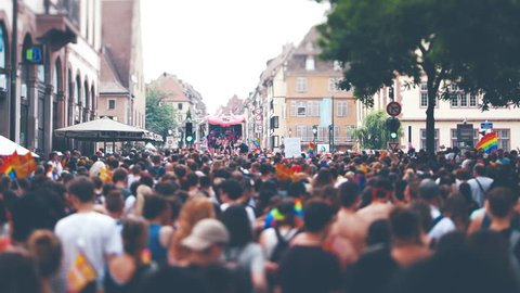STRASBOURG, FRANCE - CIRCA 2018: Cinematic color grading over large crowd of people following gay pride truck at annual FestiGays pride gays and lesbians parade marching French streets fun atmosphere