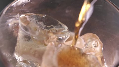 Pouring cola with ice cubes close-up. Slow motion.