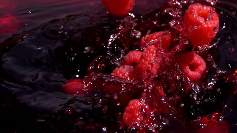 Ripe red raspberries fall into juice with beautiful splashes in slow motion