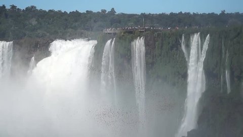People watching a swarm of birds flying in front of powerful Iguazu Falls waterfall at the border between Brazil and Argentina.