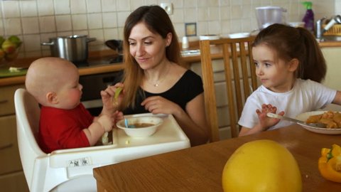 Young woman housewife feeding two children in the kitchen. Toddler and preschool girl
