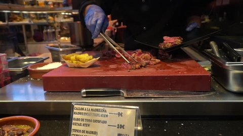 Beef tapas at San Miguel market in Madrid, Spain. You see a chef cutting cooked meat in slices