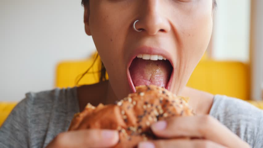 Young Hungry Woman Biting Vegan Meatless Burger in Fast Food Restaurant. Portrait of Angry Face Female Eating and Looking in Camera. 4K Slowmotion. Royalty-Free Stock Footage #1025455883